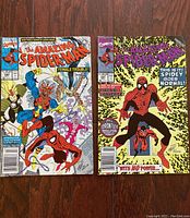 Two vintage The Amazing Spider-Man comic books lying on wooden surface showing front covers.
