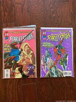 Photo showing two vintage Scarlet Spider comic books in sleeved plastic with backer-boards on wood surface. The left comic is titled The Scarlet Spider with a pink background and the right comic is The Spectacular Scarlet Spider with a purple background, both featuring action poses of the character.