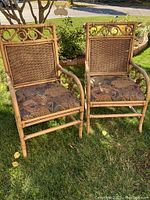 Two vintage bamboo chairs with woven rattan backs and cushions with animal print fabric upholstery shown outdoors on grass