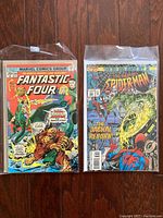 Photo shows Fantastic Four #154 and Spider-Man #36 comic books, each in clear protective sleeve with backer board, placed on a wooden floor.