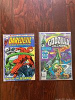Front view of two vintage Marvel comic books on wooden surface showing Daredevil and Godzilla covers.