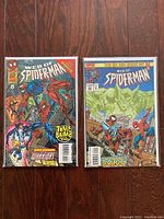 Two Web of Spider-Man comic books side by side on a wooden floor, showing colorful covers with Spider-Man and other characters.