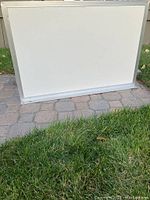 Front view of a large rectangular whiteboard with an aluminum frame and bottom ledge, placed standing on a paved surface with grass nearby.