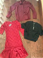 Brand new red lace dress, black textured lace jacket, and dark red dressy shirt laid flat on wood floor.