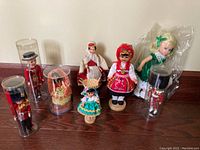 Collection of 7 assorted world dolls and figurines displayed on tabletop, including two England soldier figurines in clear cases, and 5 dolls in traditional costumes from various countries.