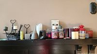 Photo showing black metal candle holders, white diffuser, multiple scented candles in jars, pillar candles in various colors, red lantern and other assorted candles on a dark wood surface.