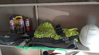 Various automotive cleaning products, microfiber mitt, gloves, black strap, and other accessories on a shelf.