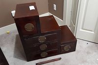 Front view of stepped chest showing top compartment, three middle drawers, one bottom drawer, brass hardware and loose front trim piece on floor