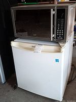 Microwave set on top of the compact refrigerator showing overall condition and relative size