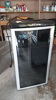 Front view of black and silver Danby Premiere wine refrigerator with glass front and visible internal racks, unplugged with power cord hanging.