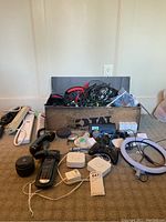 Overall lot containing extension cords, remote controls, gaming controllers, Alexa device, and assorted cables in a box and spread out