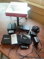View of lot showing multiple adapters, wireless devices, and cables on a wooden table.