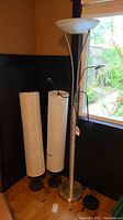 Metal floor lamp with two light fixtures and two tall cylindrical paper shade floor lamps, one with visible tears in shade