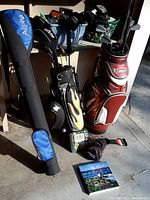 View of two golf bags, a travel carrier, golf books, and bins of golf balls and accessories.