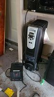 Kenwood oil-filled radiator heater in black with digital control panel photographed standing on floor near wall.