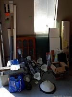 Photo shows stacked laminate flooring boxes, shelving, glass panels, lighting fixtures, and shoe rack in corner of room.