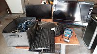 Photo showing two monitors, seven keyboards, multiple cables, surge protectors, and speakers arranged on floor.