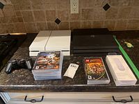 Wide shot of white PS4 Slim, black PS4 original, controller, PS3/PSP games and media remote