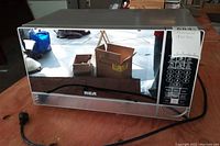 Front and side view of RCA microwave with mirrored door and black control panel on right side.
