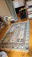 Wide angle view of the multicolor patterned decorative area rug on wooden floor with fringed edges visible.