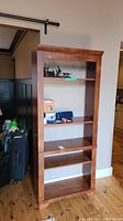 Front view of the wooden shelf unit showing three shelves with various small objects removed, shelving unit has surface scratches.