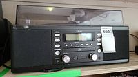 Front view of black TEAC hi-fi music system with LCD screen, buttons, rotary knobs, USB port, and dust cover for turntable.