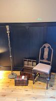 Full shot showing vintage metal floor lamp, two wooden chests, wooden chair against black wall