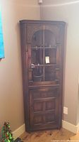 Full view of wooden corner cabinet with glass front door showing carved ornamentation and wood grain finish.