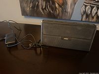 Front view of Bose SoundLink Bluetooth speaker with power adapter and cable displayed on a table.