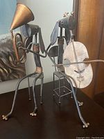 Photo showing both brass dog figurines side-by-side, one playing a horn and the other a cello.