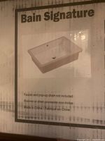 Photo of boxed Bain Signature ceramic undermount sink packaging showing product image, model info, and notes about faucet and pop-up drain not included.
