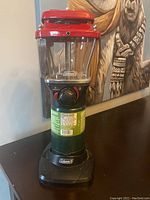 Front view of Coleman propane lantern showing propane canister, glass globe, red upper housing and control knob.