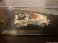 Die-cast model of 1935 Auburn 851 in cream with brown interior, displayed in a clear case with hood open to show engine details.