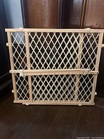 Wooden baby gate with lattice design and expandable feature shown against wooden door frame.