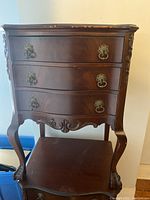 Front view of first bedside table on stand with three serpentine drawers and visible top edge chips