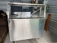 Front view of stainless steel buffet with plexiglass front and wheels at base.