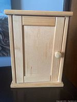 Front view of closed wooden key holder cabinet showing panel door and knob