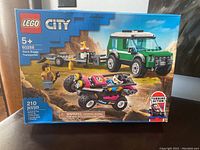 Front view of LEGO City box showing the green transporter vehicle, race buggy, and minifigures on a desert background with 210 pieces and set number 60288