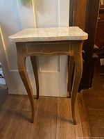 Small square side table with beige marble top and wooden cabriole legs against a white door background.