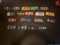 Overhead photo showing all 18 vehicles neatly arranged in rows on a black surface, displaying numbers and liveries clearly.