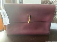 Front view of the Naturalizer Bleekley clutch showing smooth boysenberry exterior with gold-tone toggle clasp and attached brand tag.