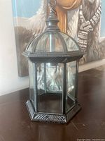 Front angled view of the hexagonal black metal framed outdoor lantern with clear glass panels and decorative top finial.