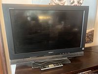 Sony 32 inch Bravia TV with screen and front showing remote control on stand under TV