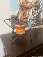 Front view of large black metal star frame candleholder with orange and red layered candle inside the center base.