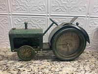 Side view of ornamental green metal tractor clock showing clock face integrated in rear wheel and detailed metal parts.