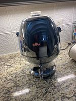 Full side view of the vintage stainless steel coffee percolator showing rounded shape, glass lid knob, side handles, and spigot at base.