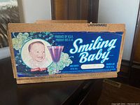 Front side of the wooden box with vintage Smiling Baby grape juice label showing the baby face and grape imagery