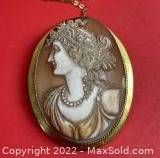 Close-up view of oval shell cameo depicting female profile set in gold bezel