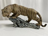 Side view of the porcelain tiger in a pouncing pose on a rock base, showing full body and detailed painting.