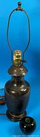Full view of the dark cloisonne vase converted into a lamp with brass lamp holder and dark wooden base, showing size reference with a green apple.